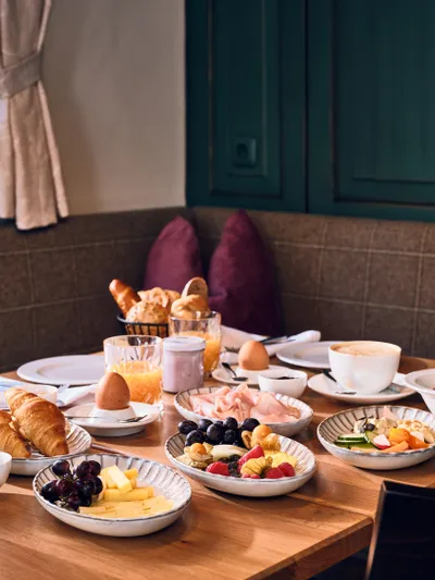 Cozy hotel breakfast table with croissants, fruit, cheese, juice, and coffee